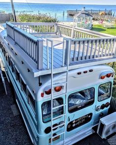 a blue and white bus parked in front of the ocean with a ladder on it's side