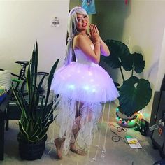 a woman in a white dress standing next to a potted plant with lights on it