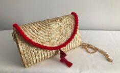 "From an evening cocktail party to a fun beach day, this straw clutch makes a graceful accessory to carry. Perfect for a summer statement. Red pom poms with red/pink tassel center.  Comes w/ removable gold chain strap that can be worn as a crossbody or shoulder strap. NOTE:  Pom pom embellishment is only on the top fold of the clutch (NOT on the back or other edges of the clutch) Details: Clutch Size: 6.5\" x 10\" Shoulder strap: 47\" gold Face material: wheat straw Lining material: polyester and cotton" Chic Red Woven Straw Bag, Bohemian Summer Evening Clutch, Beach Clutch With Tassels, Gold Straw Bag For Summer Evenings, Gold Straw Clutch Bag For Summer, Gold Straw Evening Bag For Summer, Gold Clutch For Summer Vacation, Gold Summer Vacation Clutch, Chic Straw Bag With Tassels