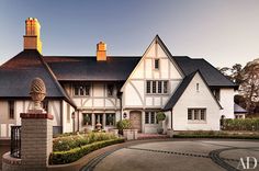 a large white house with black roof and two storyed buildings on either side of the driveway