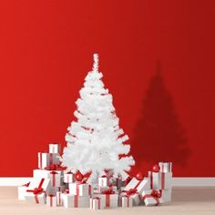 a white christmas tree surrounded by presents against a red wall