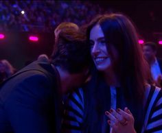 a man and woman hug each other in front of an audience at a concert or show