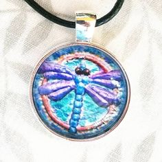 My tiny dragonfly painting is now available as a Photo Print Pendant!  I love our Mother Earth and the diversity of people, plants and animals. I strive to have all of my art reflects my environmental interest and my values.  🖤MATERIALS: They are 1 inch prints set into a round chrome bezel and covered with a round clear glass cabochon and comes on a black cord.  These are hand assembled chrome bezel with clear domed glass cabochon pendants Diameter: 1 Inch Comes with a black leather cord adjust Adjustable Hand Painted Round Necklace, Adjustable Hand Painted Necklace, Adjustable Hand Painted Necklaces, Adjustable Round Hand Painted Necklaces, Hand Painted Butterfly Jewelry Gift, Hand Painted Butterfly Jewelry For Gift, Handmade Bohemian Dragonfly Necklace, Bohemian Handmade Dragonfly Necklace, Handmade Dragonfly Necklace For Gifting