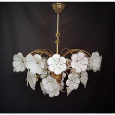 a chandelier with white flowers hanging from it's center point, against a black background