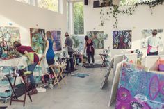 an art studio filled with lots of paintings and people working on canvases in front of large windows