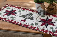 a quilted table runner on top of a wooden table next to a potted plant