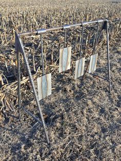 an old metal frame in the middle of a corn field with four pieces of wood hanging from it