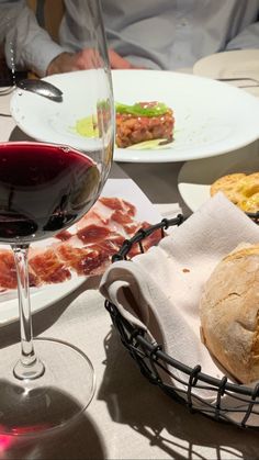 a glass of red wine and some food on a table next to a basket with bread