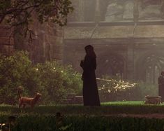 a woman standing next to a dog on top of a lush green field in front of an old building