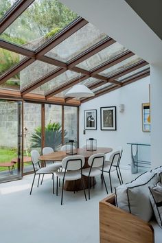 a dining table and chairs in a room with glass walls that look out onto the yard