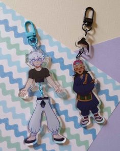 two cartoon key chains are hanging on a blue and white chevron pattern paper background