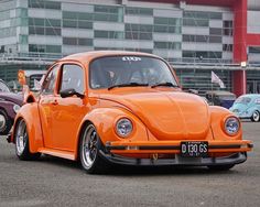 an orange vw bug parked in front of a building with other cars behind it