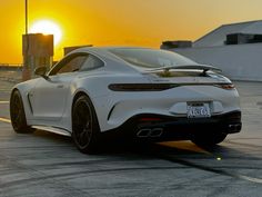 the rear end of a white sports car parked in an empty parking lot at sunset