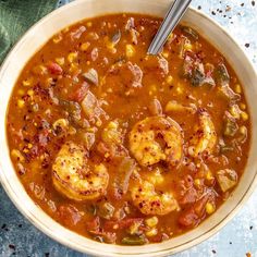 a bowl of soup with shrimp, corn and tomato in it on a blue surface