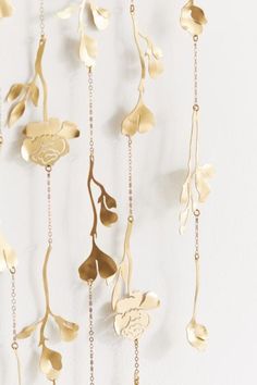 gold metal flowers and leaves hanging from chains on a white wall with chain attached to it