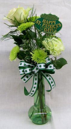 a green vase filled with flowers on top of a white cloth covered table next to a happy st patrick's day sign