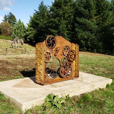 a sculpture in the middle of a field with horses grazing on grass and trees behind it