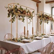 the table is set with candles, plates and flowers in gold vases on them