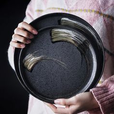 a person holding a black plate with some gold paint on it and their hands in the bowl