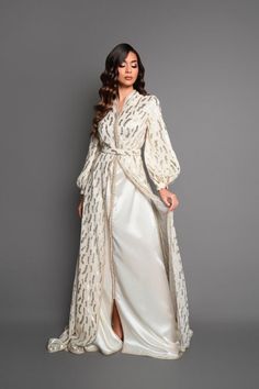 Swan neck caftan and puffed sleeves Colors: ivory subtly tinted with golden nuances The Wiheme caftan embodies timeless elegance with its swan neck and its puffed sleeves which add a touch of romanticism. Made from a light, silky fabric, this kaftan wraps you in absolute comfort. The details of Moroccan sfifa and aqaads bring cultural richness to this creation. A matching belt perfects the silhouette with finesse.  Immerse yourself in the enchanting world of the Wiheme caftan and let yourself be Elegant White V-neck Thobe, Elegant Maxi Dress For Eid, Elegant White V-neck Kaftan, Gold V-neck Kaftan For Wedding, Elegant Gold Floor-length Thobe, Elegant Long Thobe For Formal Occasions, Elegant Long Thobe For Formal Events, Elegant Long Formal Thobe, Elegant V-neck Wedding Abaya