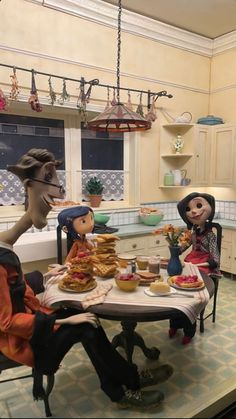 three dolls sitting at a table with food on it