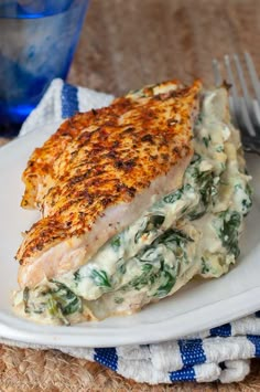 a white plate topped with chicken and spinach covered in sauce next to a fork