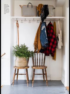 two wooden chairs sitting next to each other in front of a coat rack with coats hanging on it