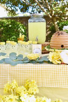 a table topped with yellow flowers next to a jar filled with liquid and lemonade