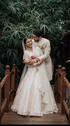 a bride and groom standing on a wooden bridge in front of some greenery at their wedding