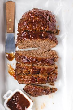 slices of meatloaf on a white plate next to sauce and a spatula