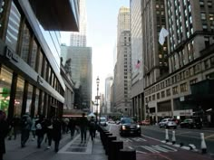 people are walking down the street in front of tall buildings and skyscrapers at dusk