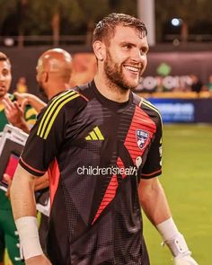 a soccer player is walking on the field with his team mates in the back ground