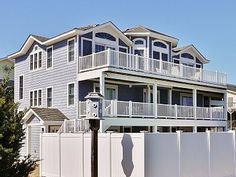 a white fence is in front of a large house with two balconies on the second floor