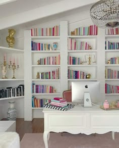 a white desk topped with a laptop computer next to a book shelf filled with books