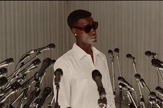 a man standing in front of a bunch of microphones wearing sunglasses and a white shirt