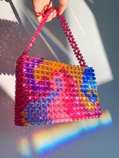 a hand holding a beaded purse in front of a white wall with light shining on it