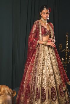 Step into refined elegance with this masterpiece in vintage reverie, showcasing a stunning tarnished gold zari embroidered lehenga. Crafted from plush gold organza tissue, it features intricate zari embroidery accented with hints of green and vintage velvet detailing. The blouse, made of rich raw silk, is gracefully embroidered with gold zari and showcases scalloping details at the hem, adorned with enchanting green bead embellishments on the sleeves. Completing this exquisite ensemble is a contrasting maroon net dupatta, adorned with meticulously crafted floral booties, epitomizing the perfect blend of luxury and artistry. Zari Lehenga, Tarnished Gold, Gold Organza, Zari Embroidery, Embroidered Lehenga, Net Dupatta, Vintage Velvet, Timeless Treasures, Red Fabric