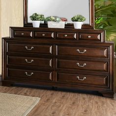 a dresser with two potted plants on top and a mirror in the corner above it