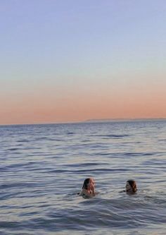 two people swimming in the ocean at sunset