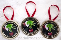 three metal christmas ornaments with red ribbon on white furnishing, one has an image of a green plant and the other says happy holidays