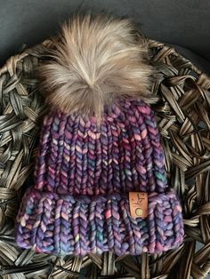 a knitted hat with a fur pom sits on top of a wicker basket