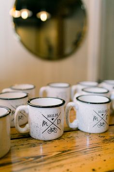 six coffee mugs sitting on top of a wooden table next to a wall mirror