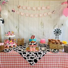 a table topped with lots of cakes and desserts next to a wall covered in balloons