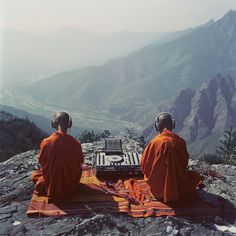 two monks sitting on top of a mountain next to each other with headphones on