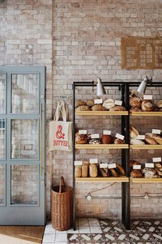 breads and pastries are displayed on shelves against a brick wall