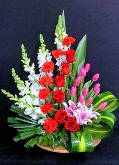 a basket filled with lots of flowers on top of a black table next to green leaves