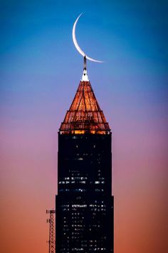 the moon is setting on top of a tall building