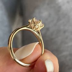 a close up of a person's hand holding a gold ring with flowers on it