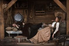 a man and woman sitting on chairs in an old fashioned room with rope hanging from the ceiling