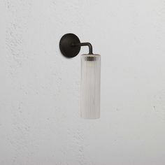 a wall mounted light on the side of a white wall with a glass tube hanging from it